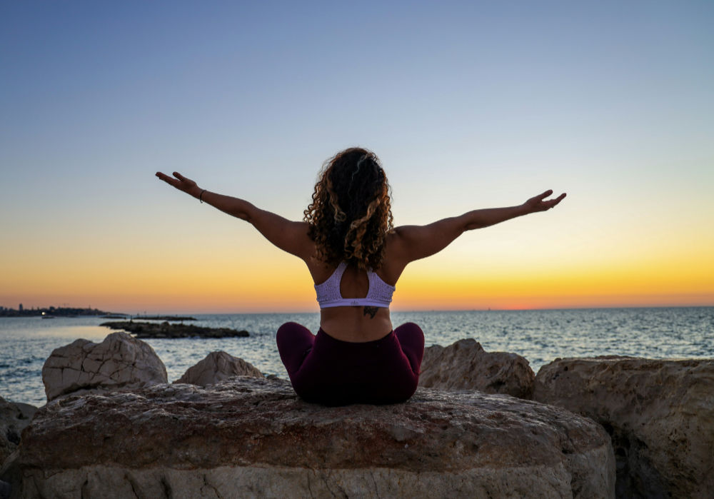 Photo d'une femme les bras ouverts face à la mer, épanouie grâce au coaching en développement personnel.